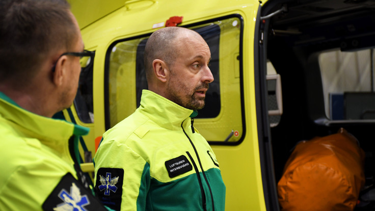 En man i en grön och gul uniform som står bredvid en gul ambulans.