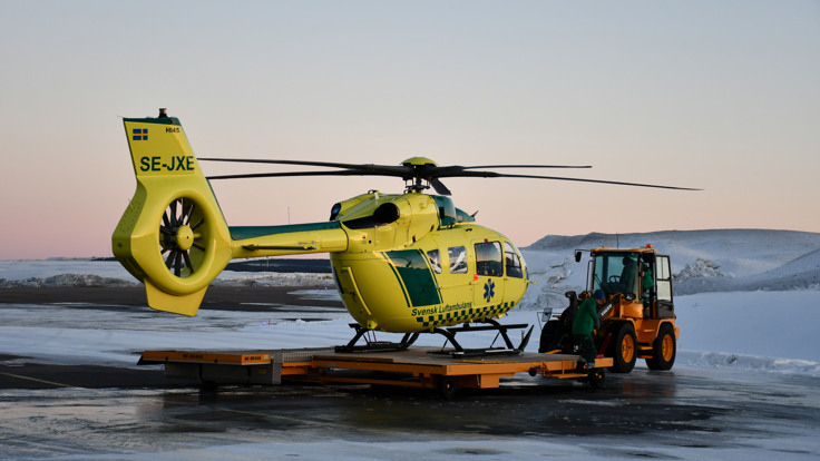 En gul helikopter som står på flygplatsens asfalterade yta.