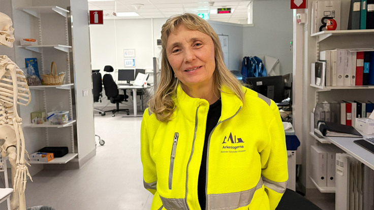 En kvinna i gul jacka står i ett kontor.