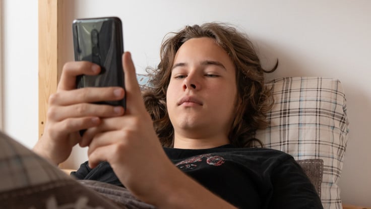 En man som ligger i sängen och håller i en mobiltelefon.