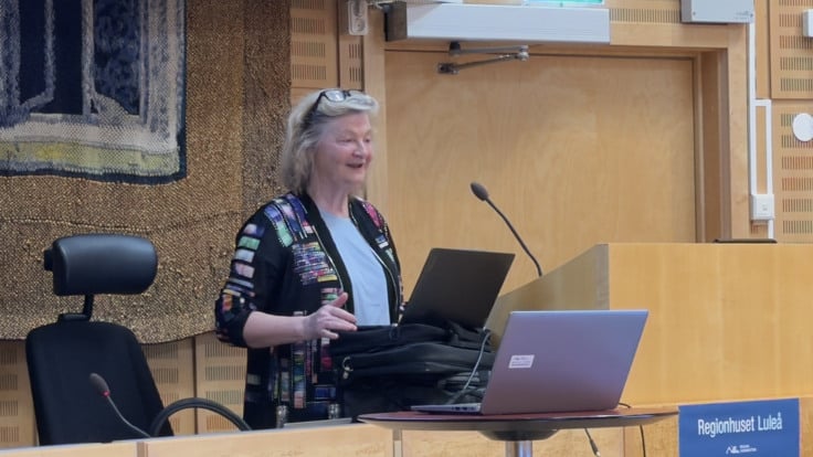 En kvinna står vid ett podium med en bärbar dator framför sig.