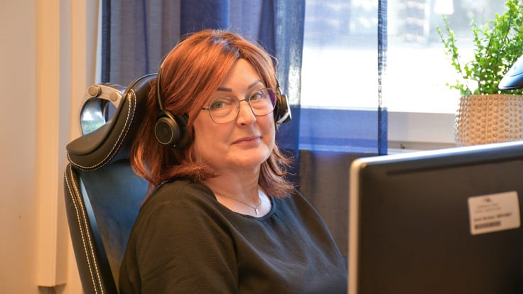 En kvinna med hörlurar sitter framför en dator.