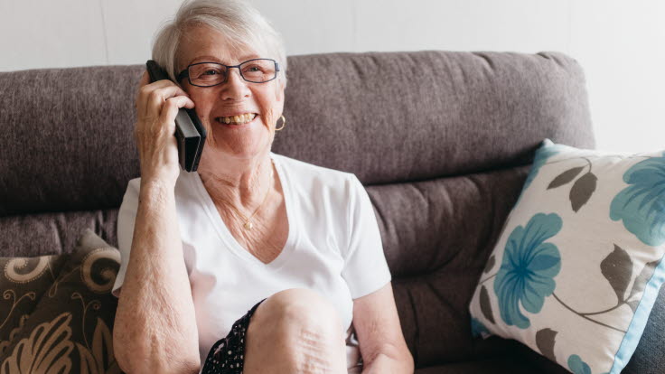 Äldre kvinna pratar i mobilen i soffan