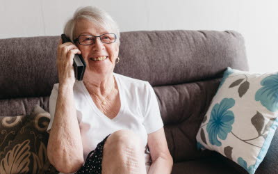 Äldre kvinna pratar i mobilen i soffan